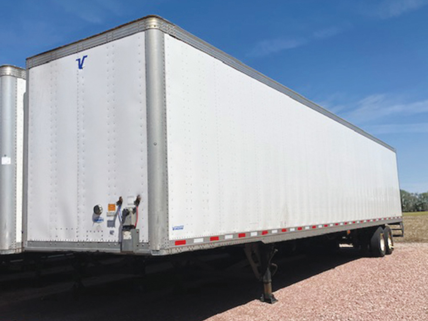 Vanguard MaxCube trailer in a side view showing white aluminum walls, front nose with V logo, wheel tires, and side underrun protection rail.