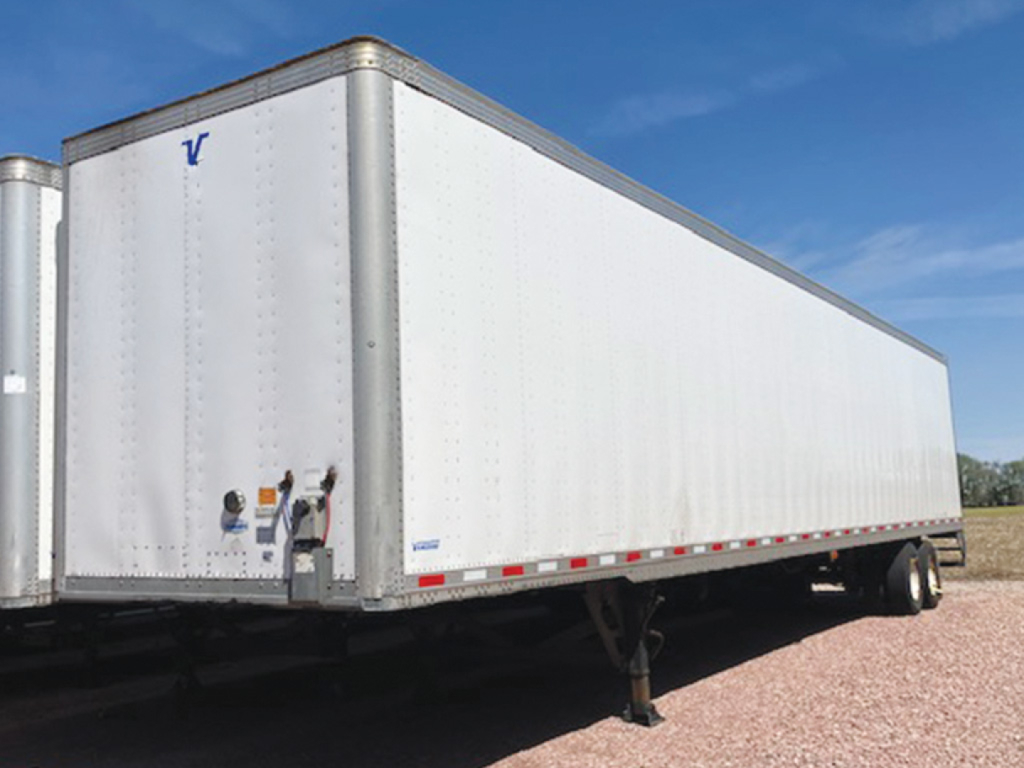 Vanguard MaxCube trailer in a side view showing white aluminum walls, front nose with V logo, wheel tires, and side underrun protection rail.