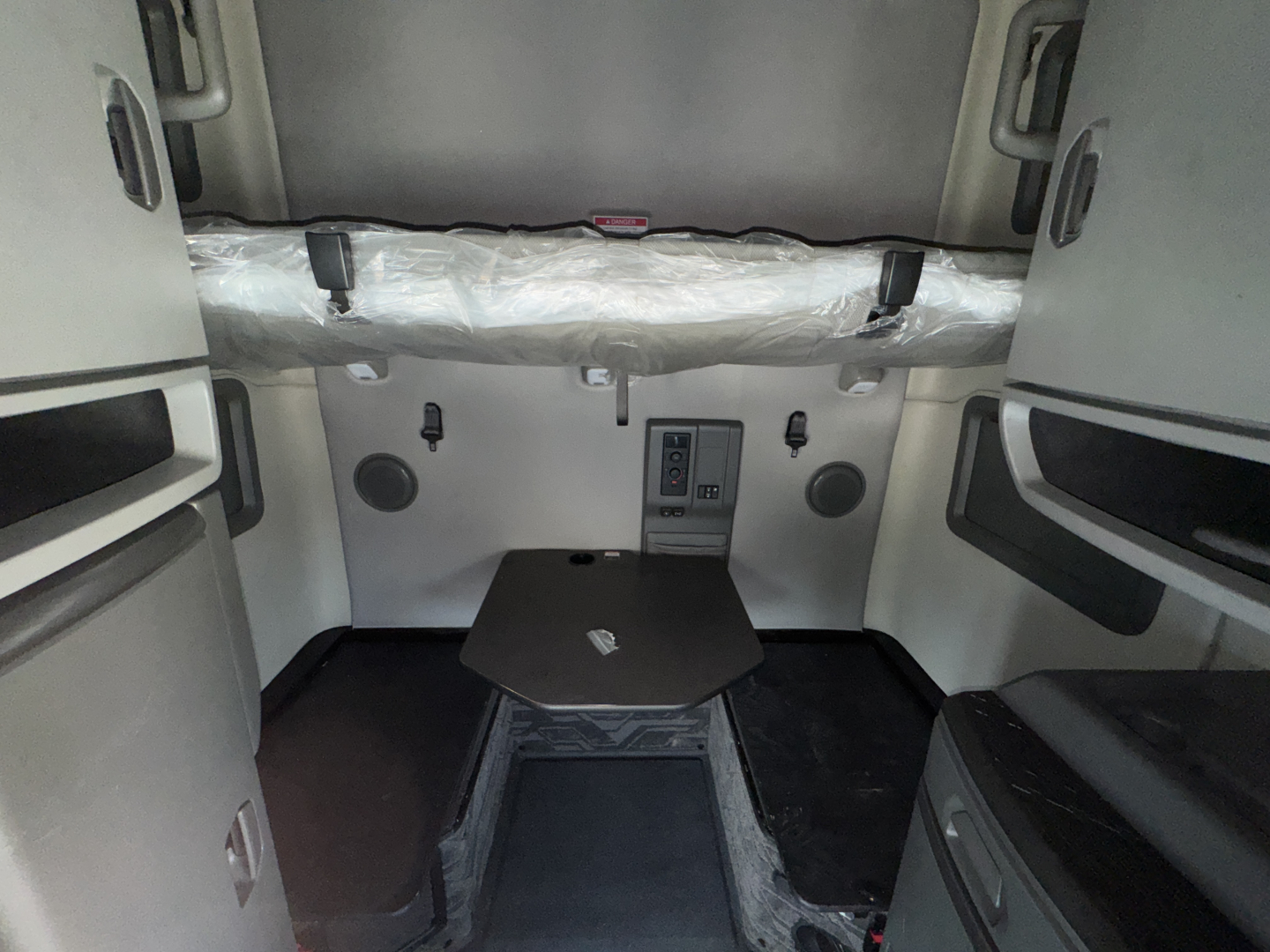 Truck cab interior of a 2023 Volvo VNL sleeper area. Visible are insulated cab wall, small table, storage cabinets, and seating. No legible labels or numbers readable in image.