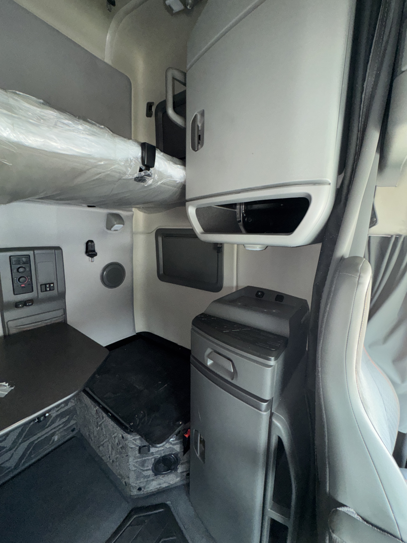 Truck cab interior showing sleeper area and storage cabinet; dashboard area visible near left; vertical console with storage drawers; gray plastic panels and step tread.