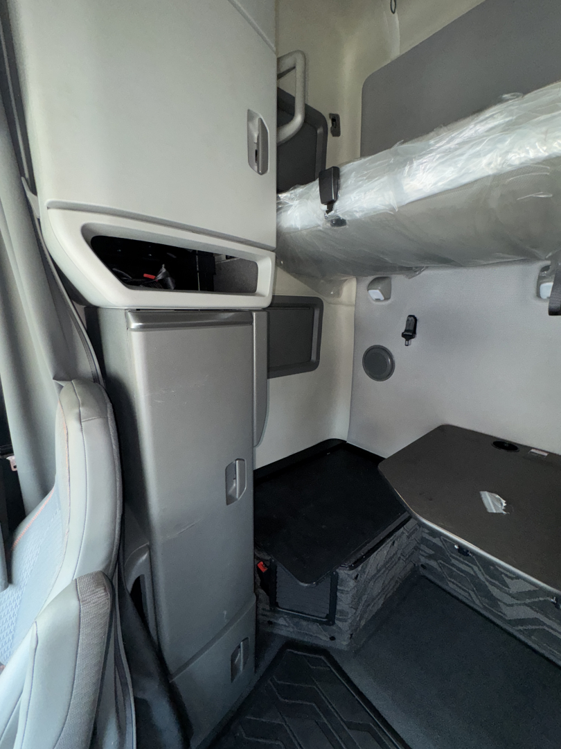 Cab interior of a 2023 Volvo VNL64T760 truck showing dashboard area, storage compartments, and a wrapped exhaust/ducting tube.