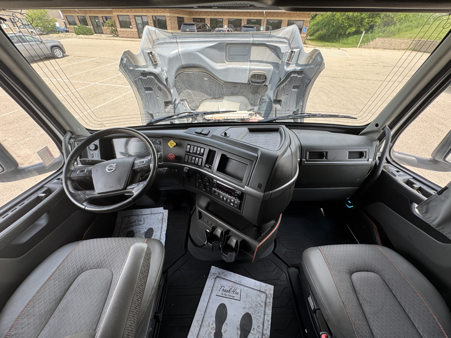 Volvo VNL64T760 cabin dashboard and steering wheel view from driver seat with open hood seen through windshield.