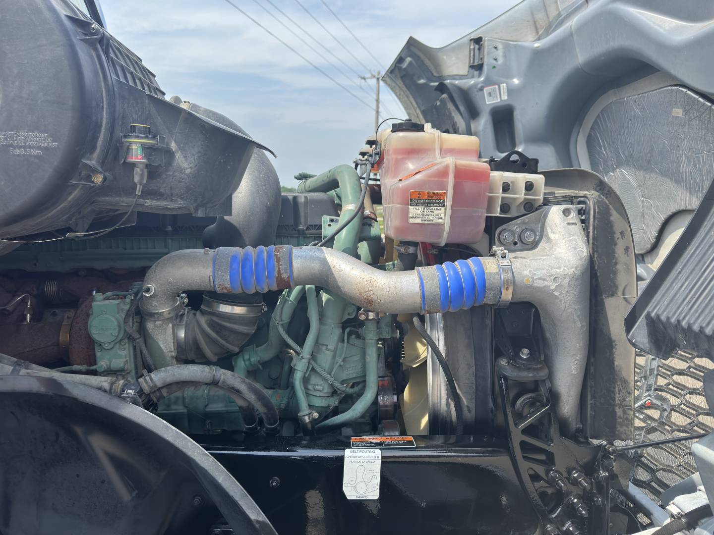 Volvo VNL64T760 engine bay showing coolant reservoir and blue hose clamps with engine components visible.