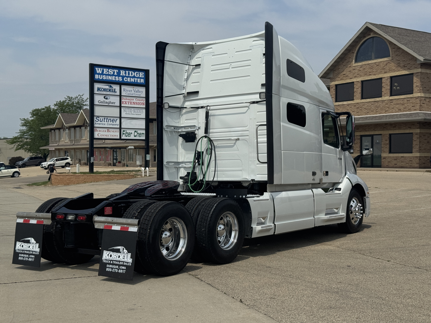 Volvo VNL64T760 tractor-trailer rear/side view showing sleeper cab, white exterior, dual rear axles, trailer kingpin area not attached, with dealership lot in background.