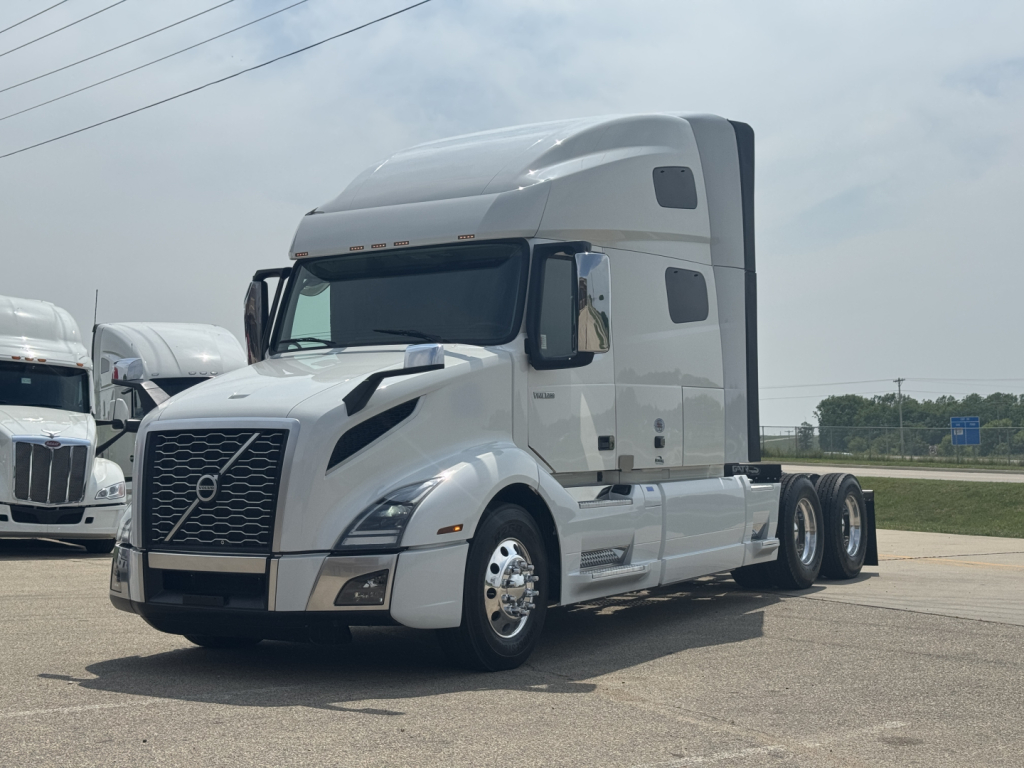 Volvo VNL64T760 truck in a dealership lot showing cab and sleeper, Volvo emblem on grille, side mirrors, and chrome wheels.