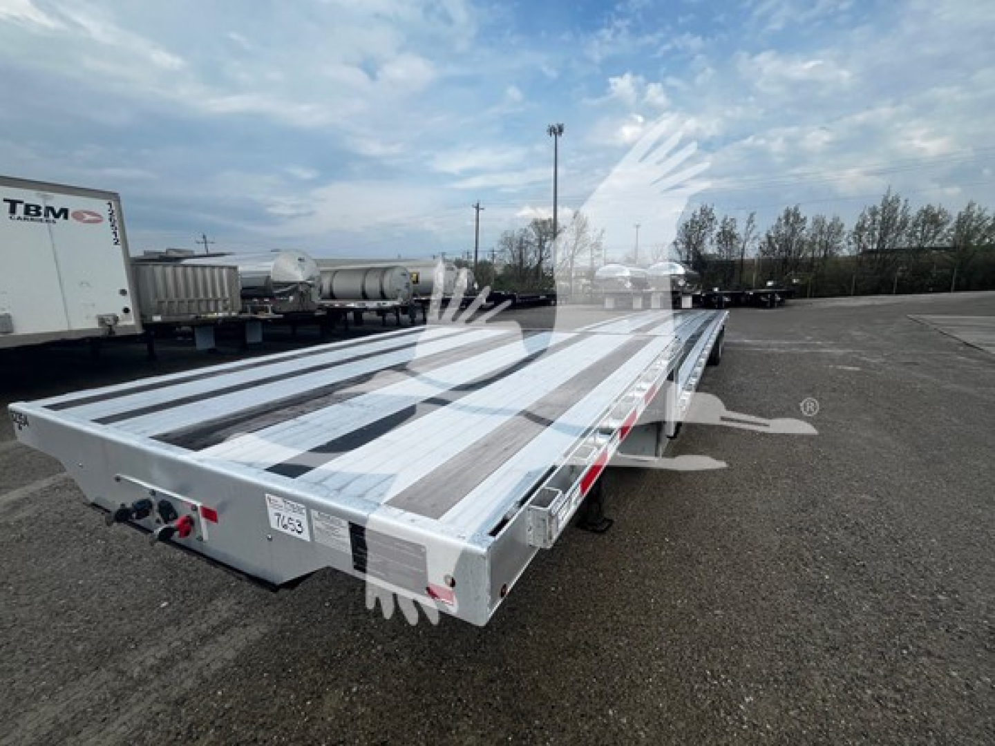Transcraft aluminum drop deck trailer viewed from rear-left, showing open deck with aluminum planks and undercarriage.