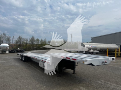 Transcraft aluminum drop deck trailer in a yard, low-angle view showing long flat deck with dual rear axles and rear ramps.
