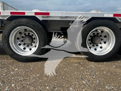 Trailer axles and wheels of a 2023 Transcraft aluminum drop deck trailer showing two rear dual tires and metal deck edge.