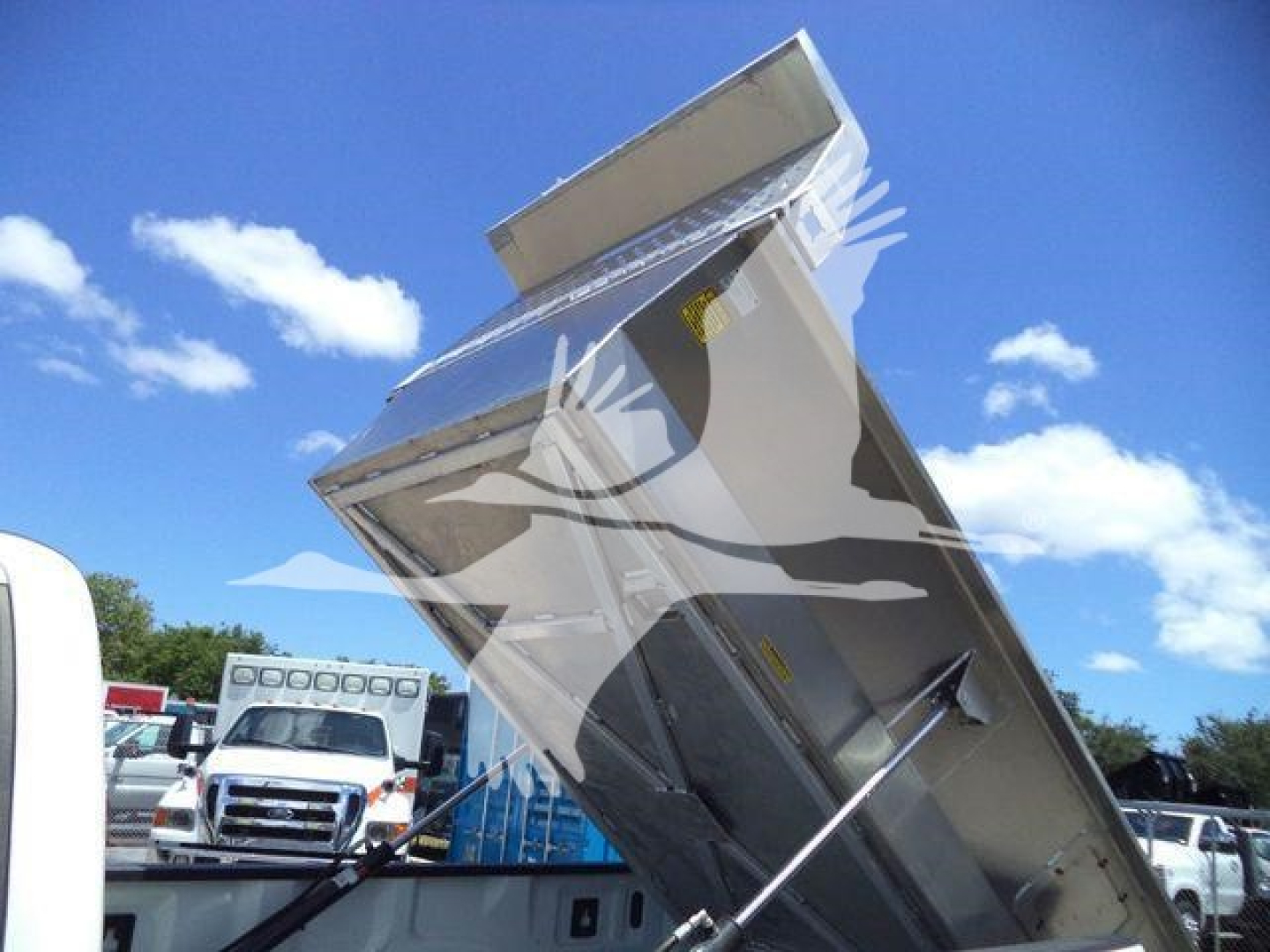 Front view of a Volvo 8 ft dump body truck bed angled upward, with open tailgate and hydraulic support, on a bright day.