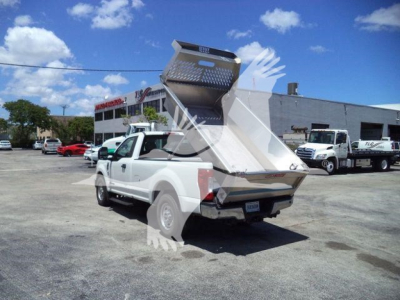 Truck bed with aluminum dump bed raised on a Volvo truck showing ALUMVOTH8DMP stock; other trucks in lot.