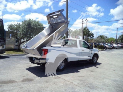 Truck bed with a dumped aluminum dump bed raised on a white pickup truck, showing the hydraulic mechanism and mesh gate.