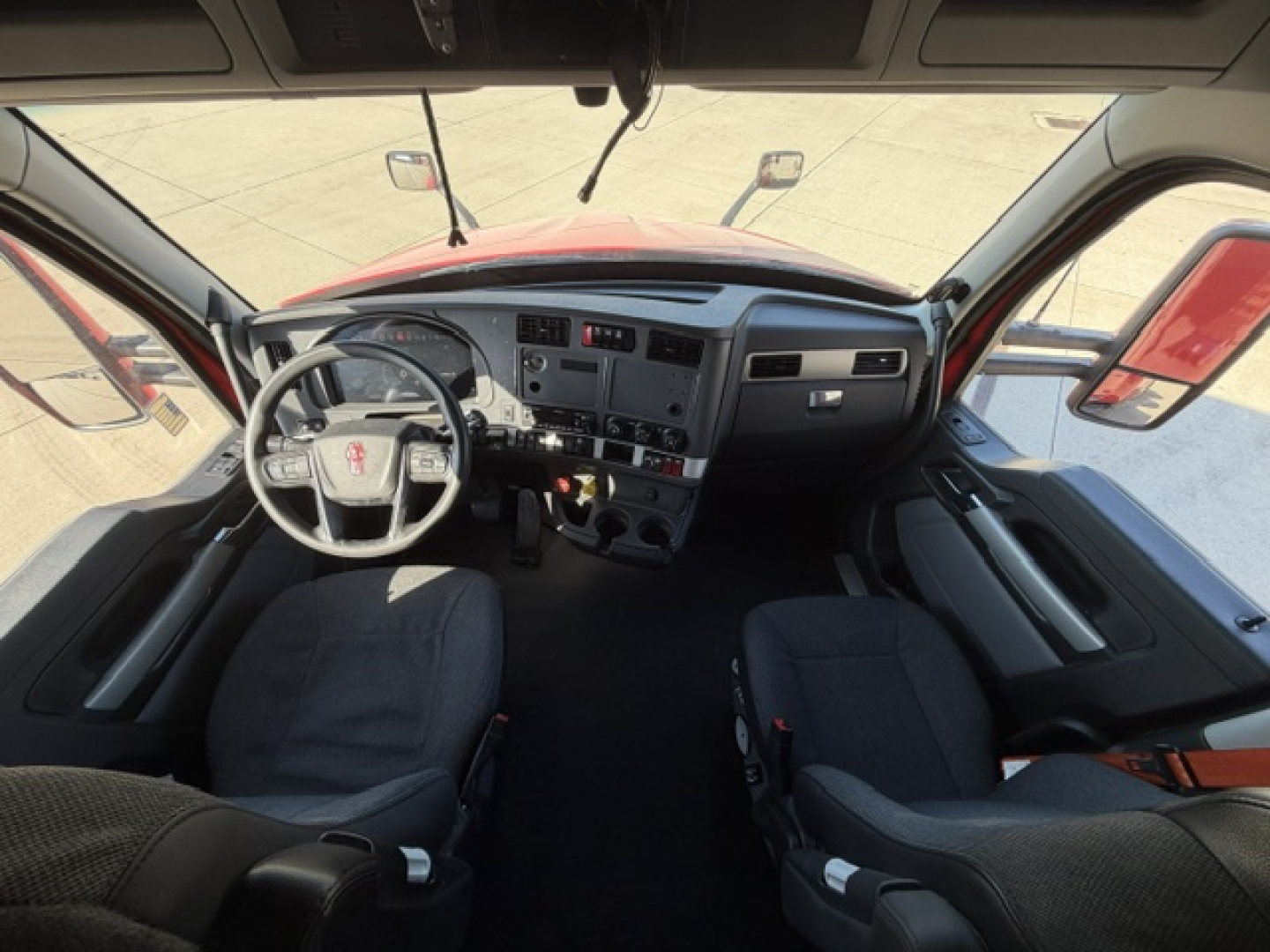 Kenworth T680 interior cabin view from front seats showing steering wheel, dashboard, and center console with gauges and controls.