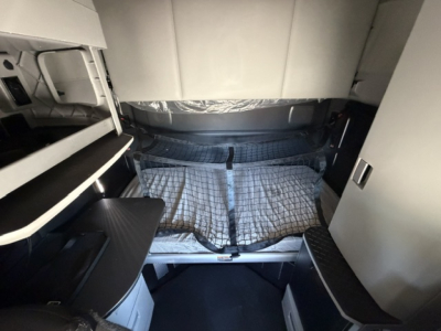Interior sleeper cab of a truck showing a bed with quilted cover and surrounding cabinets; no legible labels or numbers visible.