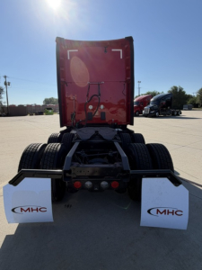 Kenworth T680 tractor rear view showing dual rear axles, fifth wheel frame, and mud flaps with MHC logos.