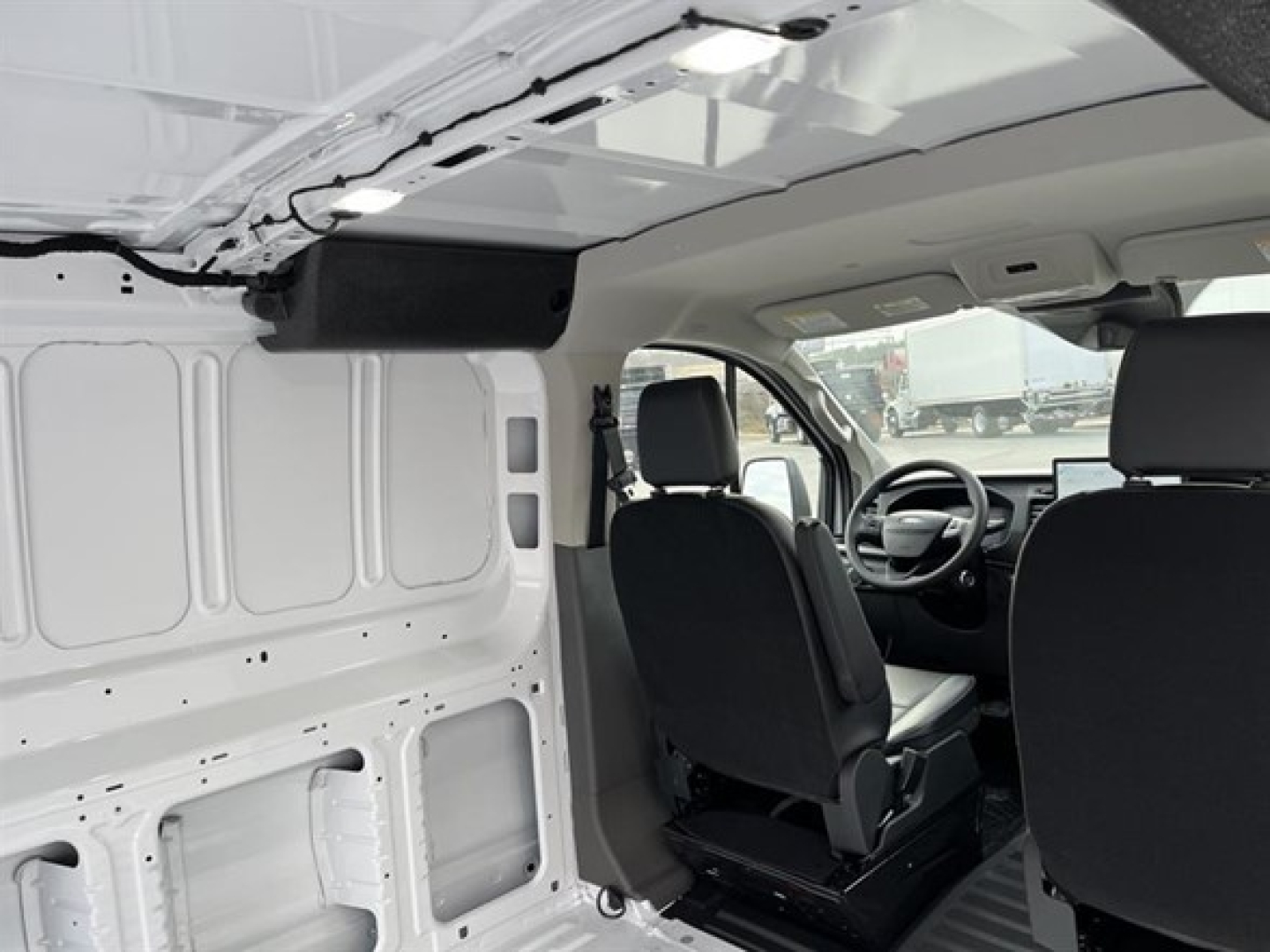 Transit cargo van interior showing front seats and cargo area with white walls and panels.