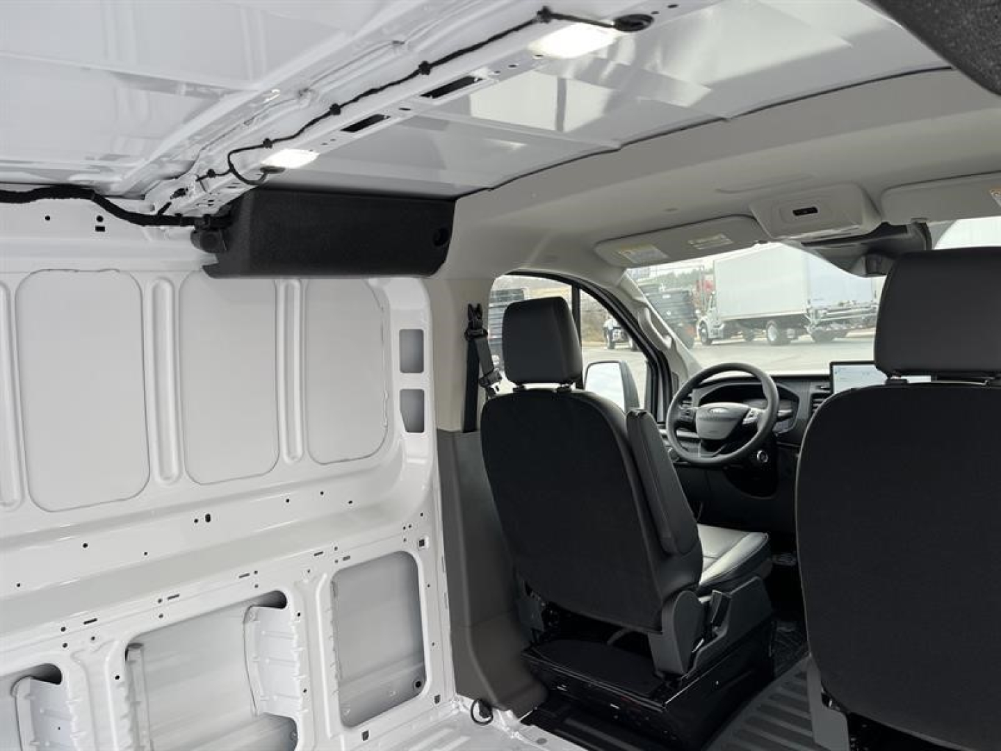 Ford Transit cargo van interior view showing driver and front passenger seats, cargo area with white panels and exposed metal framing.