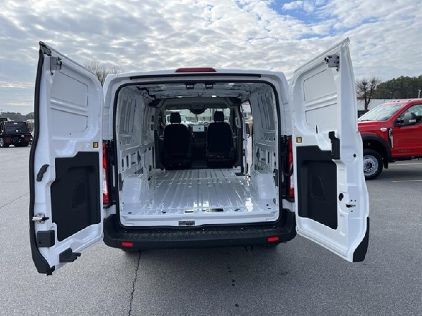 Ford Transit cargo van with rear double doors open, showing empty cargo area and front seats visible through to the cabin.