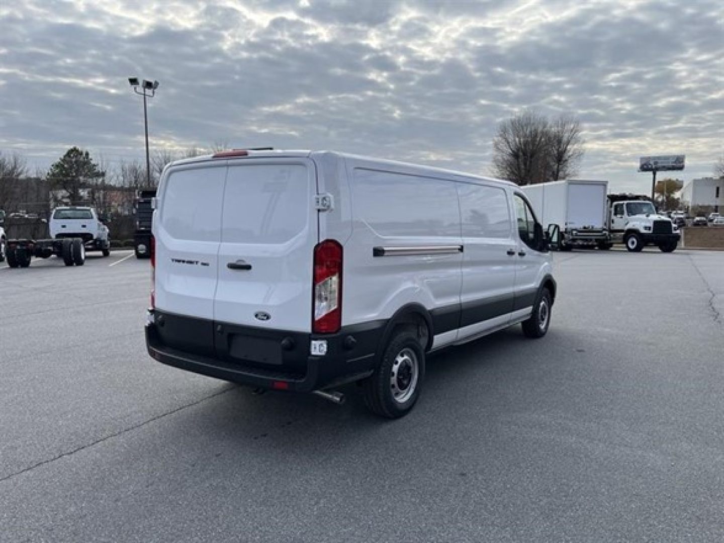 Ford Transit cargo van rear-left view showing white body, black bumper, tail lights, and dual rear doors; VIN and stock number not visible on the vehicle.