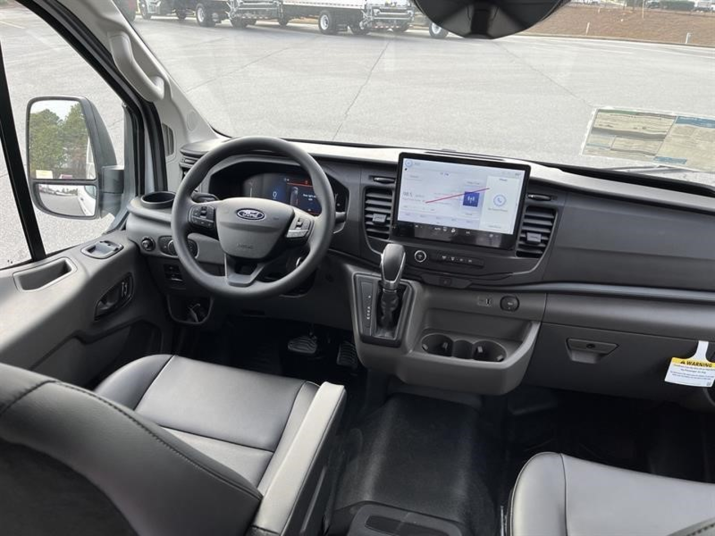 Ford Transit cargo van interior showing steering wheel, dashboard with tablet infotainment display, gear selector, and front seats.