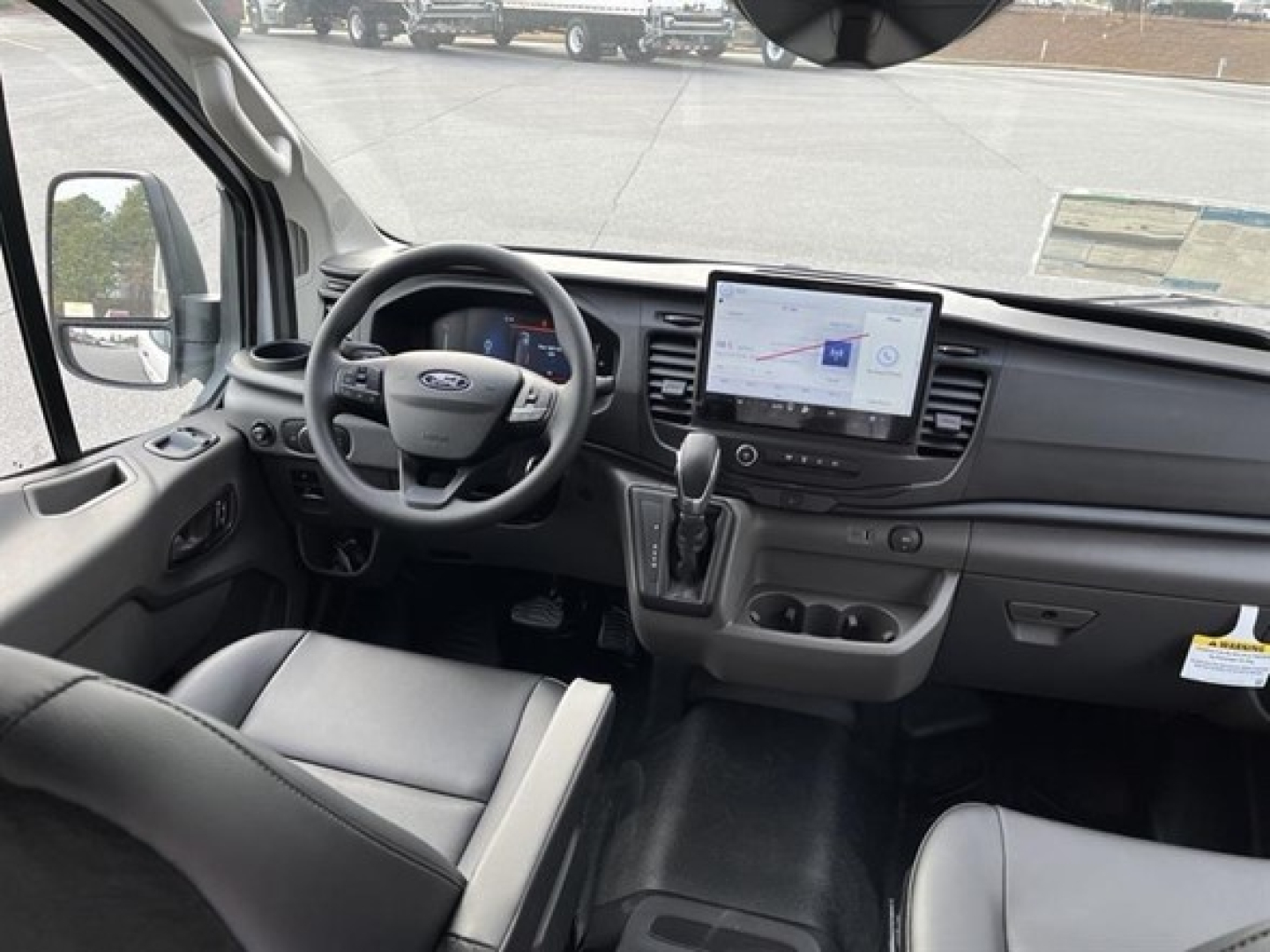 Ford Transit cargo van interior showing steering wheel, large touchscreen display, gear selector, and dashboard controls.