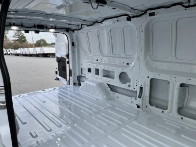 Transit van cargo interior with bare metal walls, wheel wells, and ribbed floor seen through side door.
