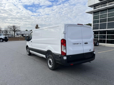 Ford Transit cargo van rear-right view showing blank white side panels and Ford badge on tailgate, exterior lighting, black bumper, no visible branding besides Transit logo.