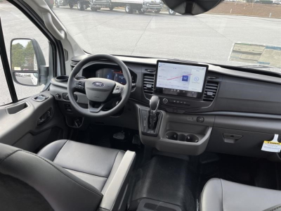 Ford Transit cargo van interior showing steering wheel, dashboard with tablet infotainment display, gear selector, and front seats.