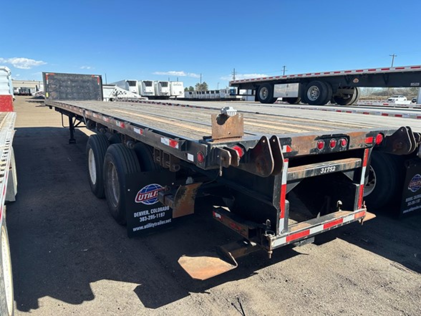 Flatbed trailer showing metal platform and rear undercarriage with red-and-white reflective tape and dual rear wheels.