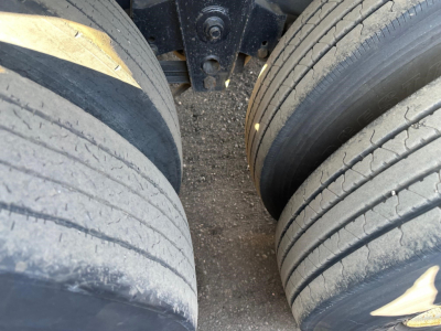 Flatbed trailer undercarriage with dual rear tires and suspension components visible.