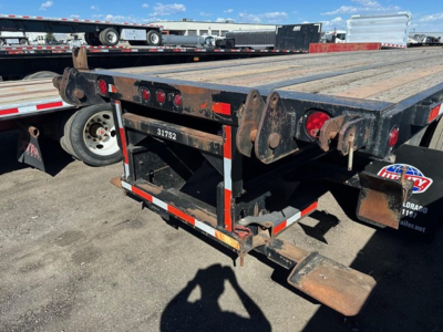 Trailer rear showing flatbed with rusted steel deck, taillights, and rear bumper. Visible numbers 31752, UE11422 stock tag, and hydraulic/suspension components.