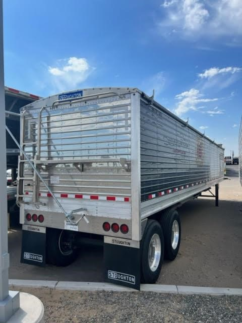 Stoughton Ag hopper trailer in side/rear angle showing aluminum panels, rear gate, taillights, and dual axles with Stoughton mudflaps.
