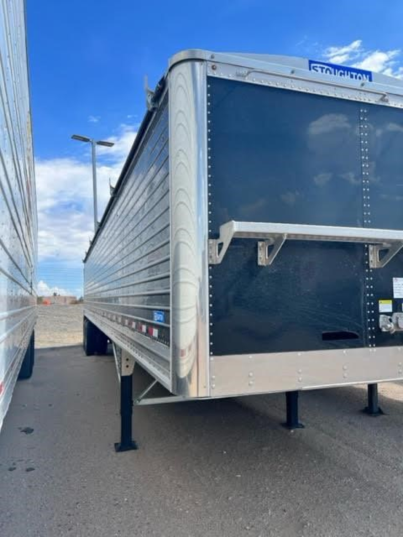 Stoughton Ag hopper trailer side and front showing aluminum corner guards and rear frame; blue dark trailer with riveted panels and front jack stand.