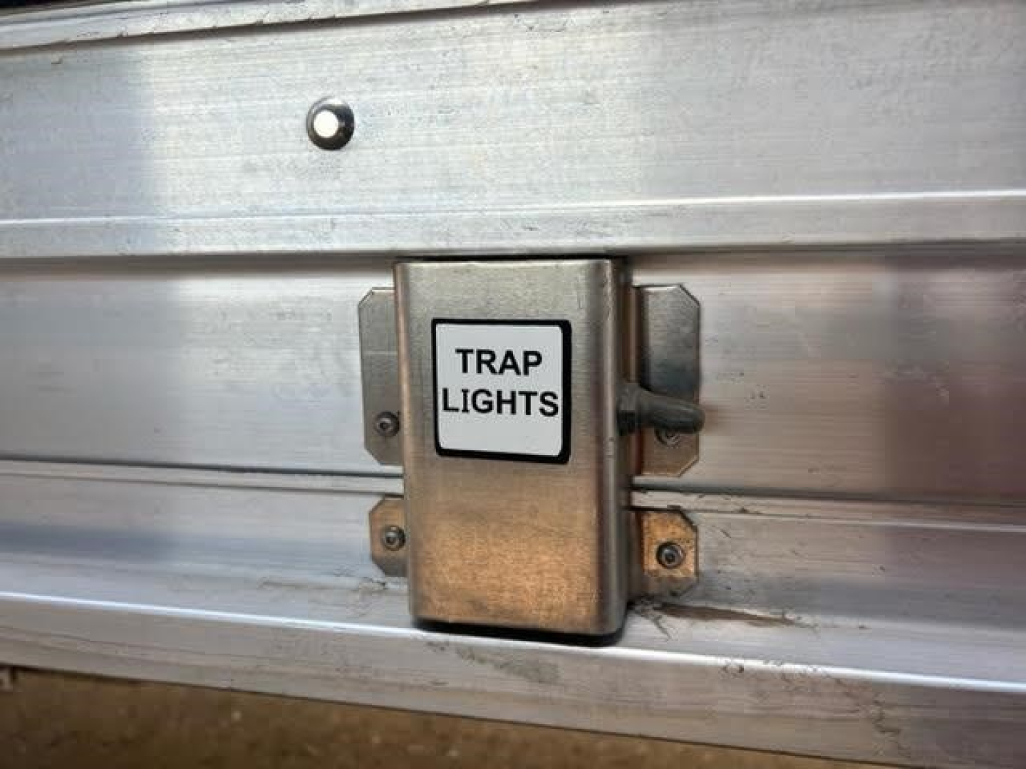 Hopper trailer side showing a metallic electrical box labeled TRAP LIGHTS mounted on the side with two mounting brackets.