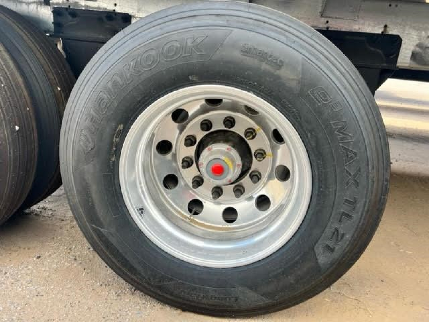 Trailer wheel with Hankook Dynap Power steering? The visible text on tire reads 'D M A X TL?'. Rim has multiple lug nut holes and a red center cap. The wheel is mounted on a trailer axle.