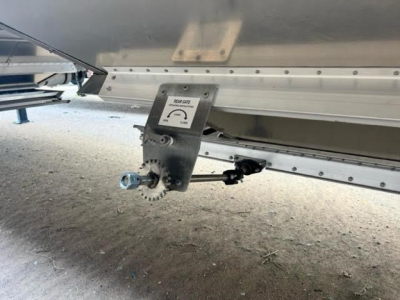 Trailer underside showing hitch mechanism and silver transfer hopper body with textured surface and bolts.
