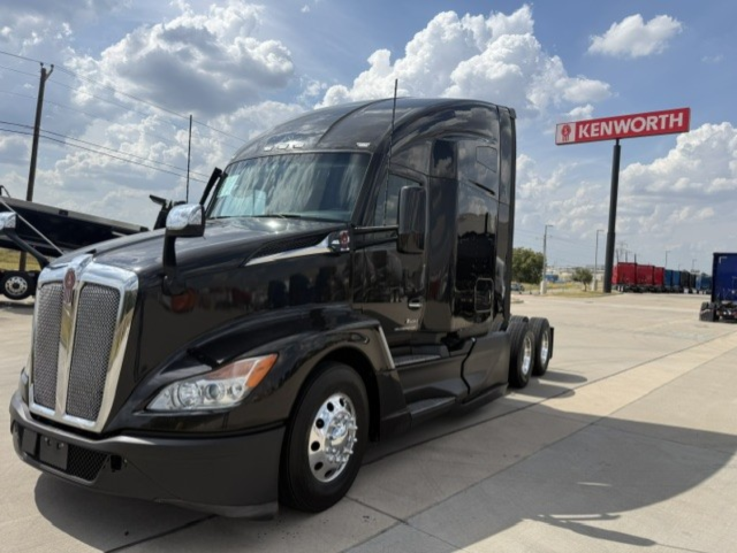Kenworth T680 in-service black tractor with large grille and dual rear axles at a dealership lot.