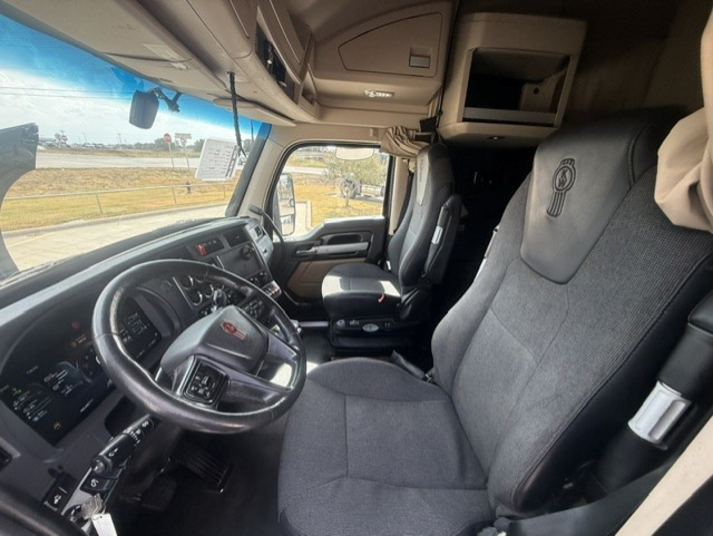Kenworth T680 cabin interior showing steering wheel, driver seat, and dashboard with controls.