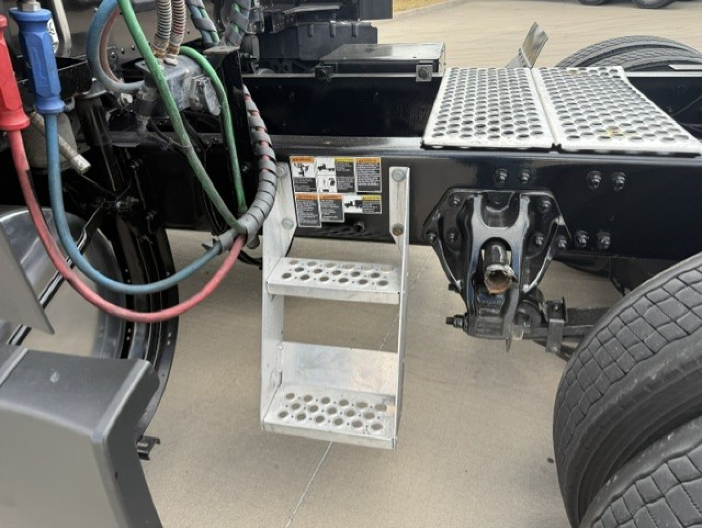 Kenworth T680 truck chassis shown with aluminum steps, hydraulic lines, and mounting area near the driver side.