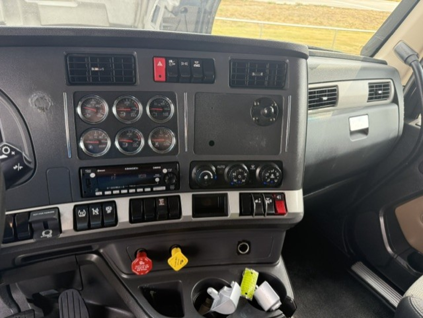 Kenworth T680 dash interior showing instrument cluster, knobs and switches, center console with circular gauges, vent panels, and control dials.