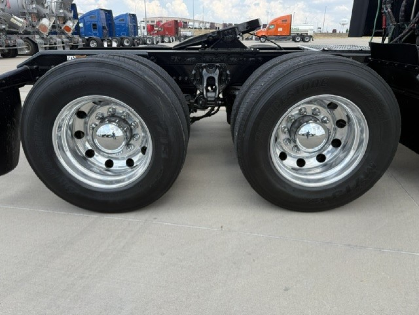 Kenworth T680 chassis dual rear wheels showing chrome rims and tire treads, frame rails and suspension components visible.