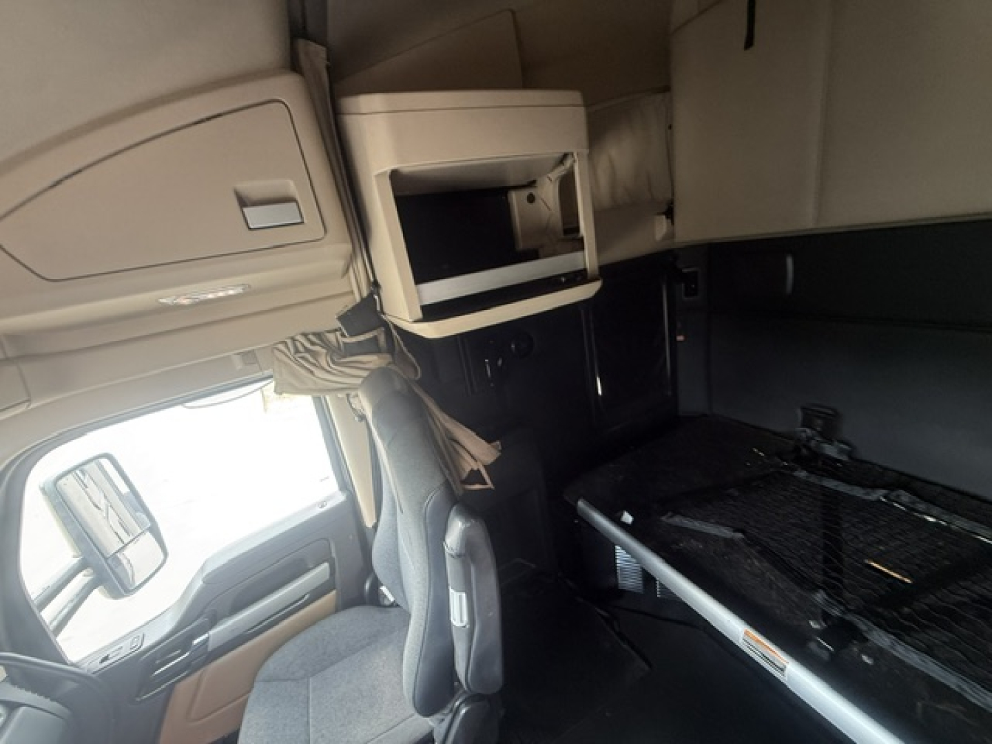 Kenworth T680 truck interior cab area showing sleeper bunk window, overhead storage cabinet, and bedding surface; left-side view from driver seat.