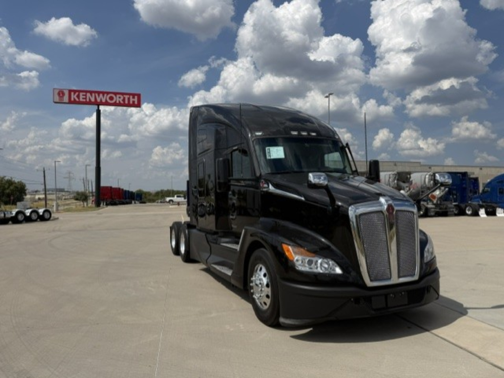 Kenworth T680 tractor-trailer in a dealership lot; front view showing large chrome grille, black cab, and Kenworth sign in background.