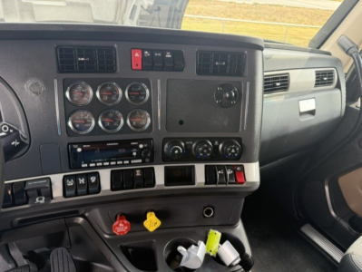 Kenworth T680 dash interior showing instrument cluster, knobs and switches, center console with circular gauges, vent panels, and control dials.