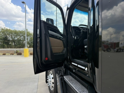 Truck cab and open door of a 2023 Kenworth T680 showing entry step, interior seat, and door panel with materials; side mirror and front wheel visible.
