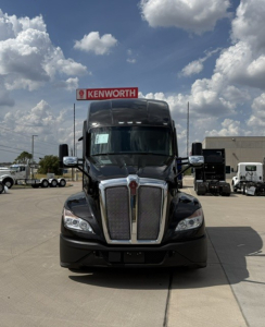 Kenworth T680 truck front view in a dealership lot with Kenworth sign in background.