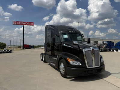 Kenworth T680 tractor-trailer in a dealership lot; front view showing large chrome grille, black cab, and Kenworth sign in background.