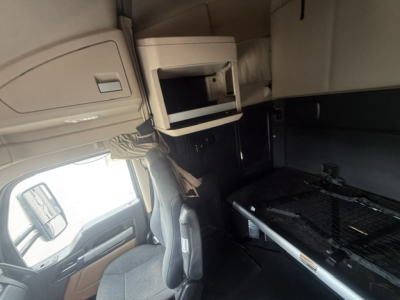Kenworth T680 truck interior cab area showing sleeper bunk window, overhead storage cabinet, and bedding surface; left-side view from driver seat.