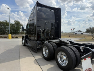 Kenworth T680 side view showing tractor cab with dual rear axles and fifth wheel, black exterior, visible warning decals, chrome wheels.
