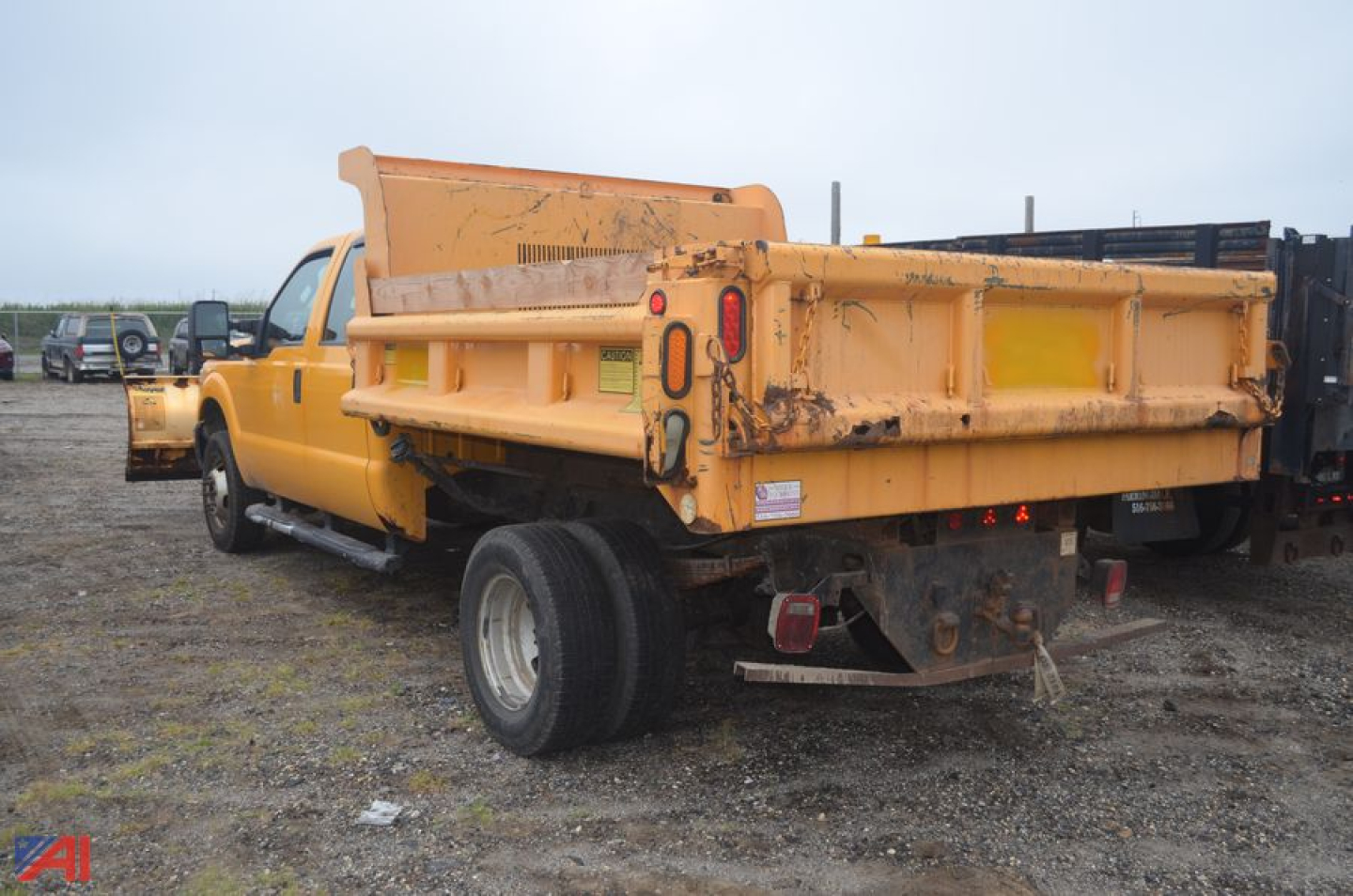 Dump truck bed and plow attachment on a yellow Ford F-350 Super Duty dump truck, rear view showing tailgate and plow mount.