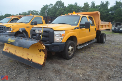 Ford F-350 Super Duty dump truck with plow blade in foreground, yellow body, dump bed raised, parked in lot with other yellow trucks.